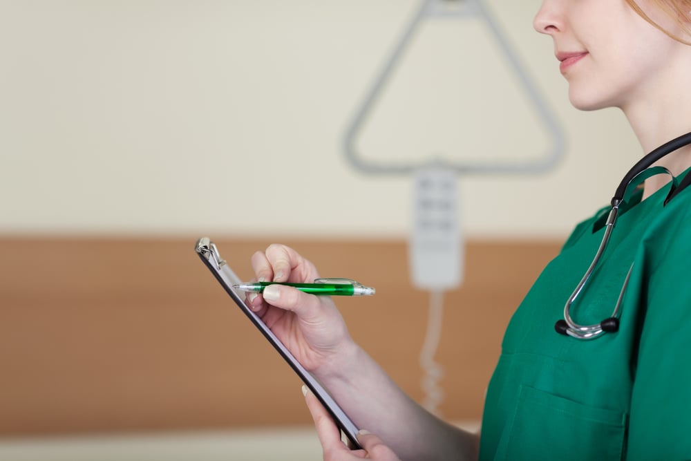 Close up of the profile of a young female doctor or nurse taking patient notes on the ward