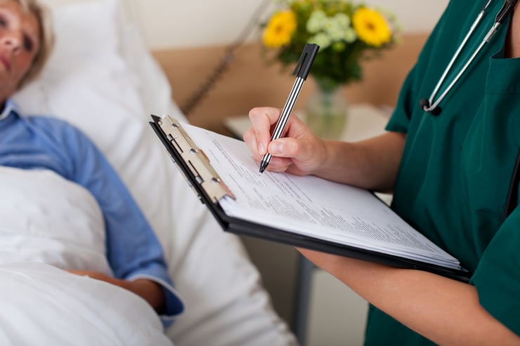 Writing on clipboard with patient in background in hospital-1
